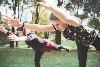 Sabahın köründe parkta yoga yaparak antrenman yapan iki genç kadın. 