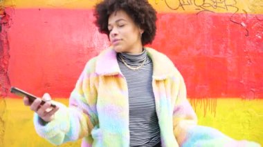 Genç ve güzel kıvırcık saçlı siyah kadın şehirde dans ediyor. Akıllı telefon kullanıyor. Kendini özgür hissediyor ve iyi bir günü kutluyor.