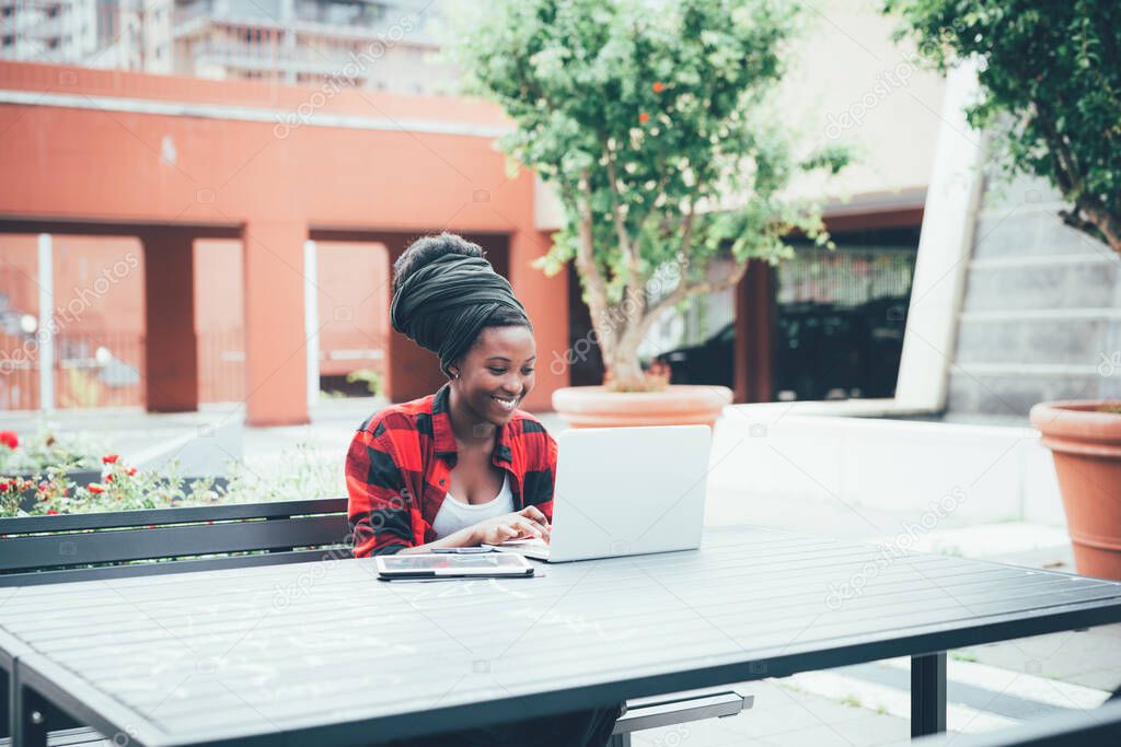 Young black woman using computer sitting outdoor remote working and studying for college