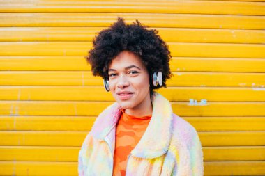 Kulaklık takmış, açık havada poz veren kıvırcık saçlı genç bir kadının portresi.