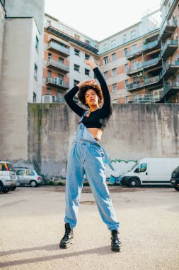 Genç melez kıvırcık saçlı kadın dışarıda dans ediyor.