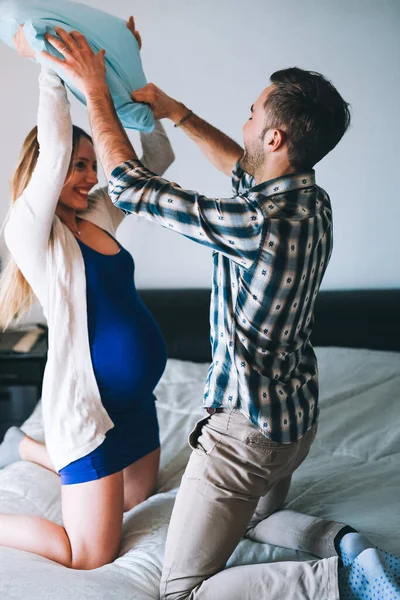 Genç hamile çift yatak odasında yastık kavgası yapıyor. Birlikte eğleniyorlar.