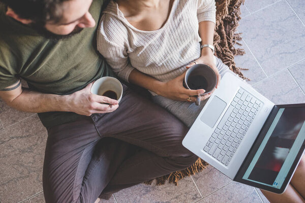 Young multiethnic couple using pc having coffee