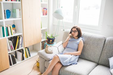 Yetişkin bir kadın koltukta oturup klasik telefonlardan konuşuyor.