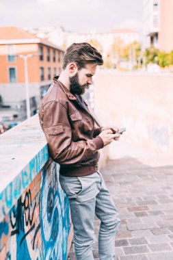 Young bearded man outdoor using smartphone home banking clipart