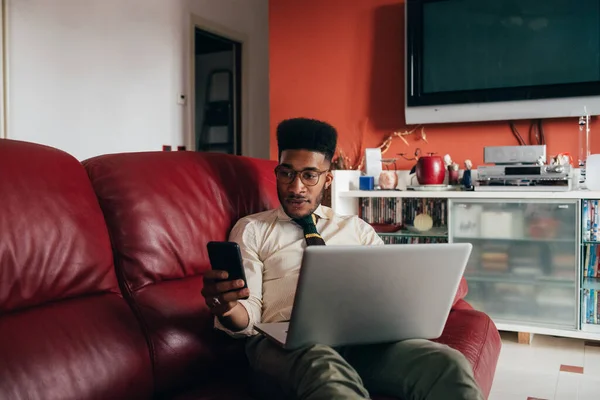Joven Hombre Negro Interior Sofá Tumbado Casa Utilizando Ordenador Teléfono — Foto de Stock