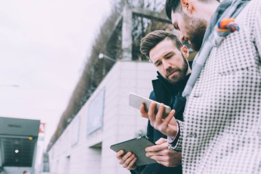 Açık havada akıllı telefon tableti kullanan iki genç işadamı.