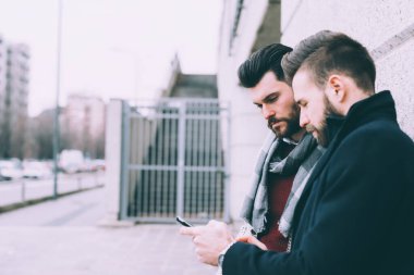 İki başarılı sakallı iş adamı akıllı telefon kullanıyor.
