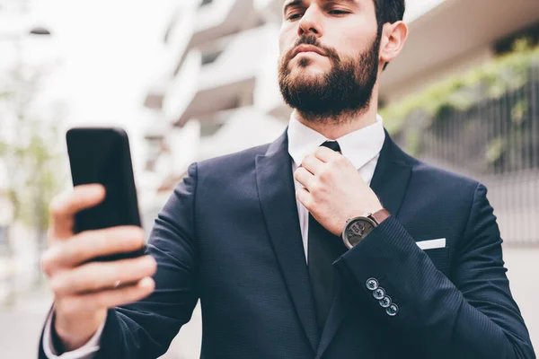 Young Bearded Contemporary Businessman Using Smart Phone Fixing Tie Doing — Stock Photo, Image