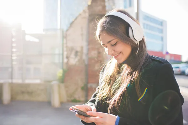 在室外使用智能手机 戴耳机听音乐或观看视频流的年轻女性 — 图库照片