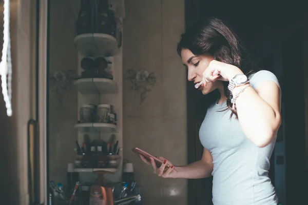 Wanita Muda Dalam Ruangan Rumah Menyikat Gigi Menggunakan Pesan Smartphone — Stok Foto