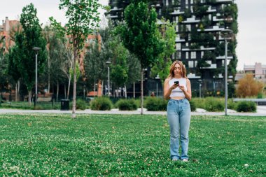 Beyaz kadın dışarıda akıllı telefon mesajları kullanıyor ya da internetten video izliyor.