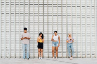 Küçük grup çok ırklı arkadaşları dışarıda akıllı telefon kullanıyor. Reklam alanının en üst düzey olduğu duvarı görmezden geliyorlar.