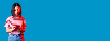 Tecrit edilmiş Asyalı genç bir kadın internet üzerinden akıllı telefon sörfü yapıyor ya da video izliyor - kesilmiş afiş reklamları yapıyor