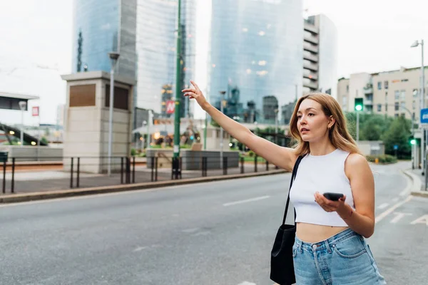 Young Woman Outdoors Hailing Taxi Holding Smartphone Hitching — Stok fotoğraf