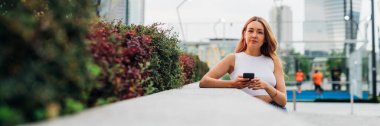 Young caucasian woman outdoors using smartphone looking over serene and positive - advertising copyspace banner