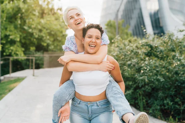 Dışarıda kucaklaşan iki genç kadın sırtına binip gülümsüyor.