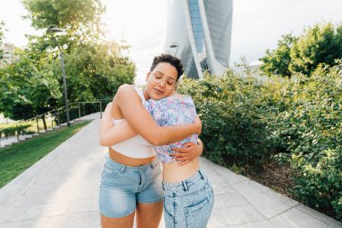 Dışarıda kucaklaşan iki genç kadın neşeli bir şekilde birbirlerine bağlanıyorlar.