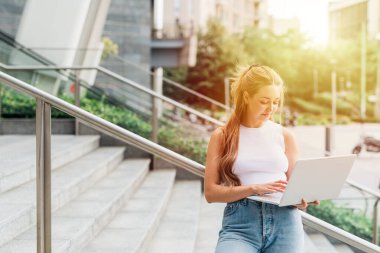 Beyaz tenli esnek işçi dışarıda bilgisayar tutuyor, uzaktan arka planda çalışıyor.