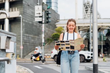 Genç beyaz kadın fotoğrafçı elinde turist haritası olan gezgin gülümseyerek etrafı geziyor.