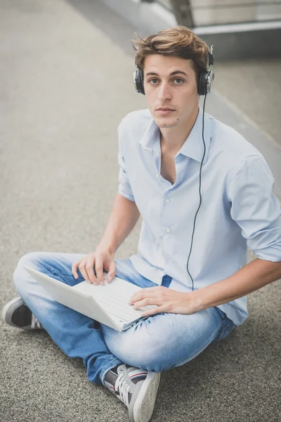 Joven modelo hansome hombre rubio con portátil y auriculares —  Fotos de Stock