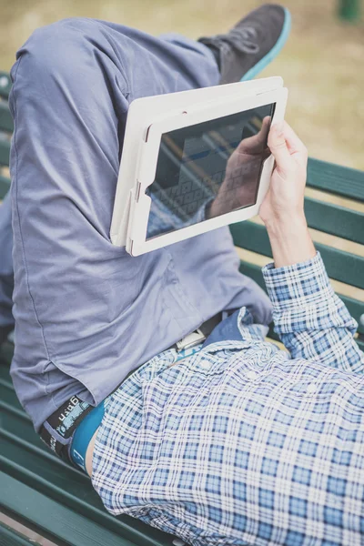Cerrar las manos hombre usando la tableta acostado en un banco —  Fotos de Stock