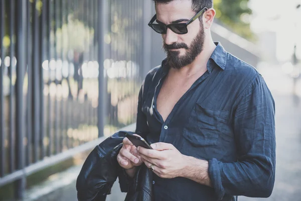 Молодой красивый привлекательный бородатый модель мужчина с помощью смартфона — стоковое фото