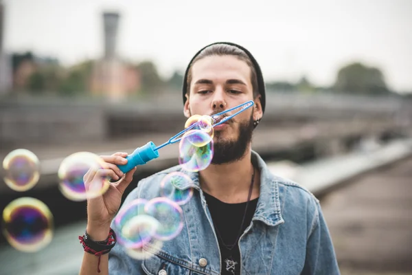 Jovem bonito barbudo hipster homem soprando bolhas sabão — Fotografia de Stock