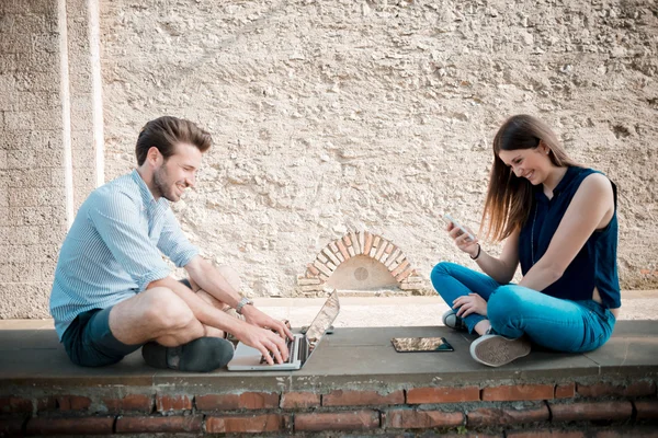 Mladý pár pomocí technologie multitasking smarpthone tabletu a — Stock fotografie
