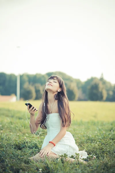 Beautiful young woman with white dress listening music — Stock Photo, Image