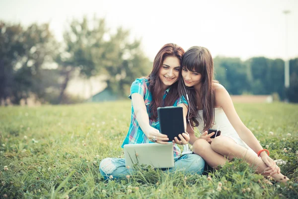 Sisters using tablet and smartphone in the park — Stock Photo, Image