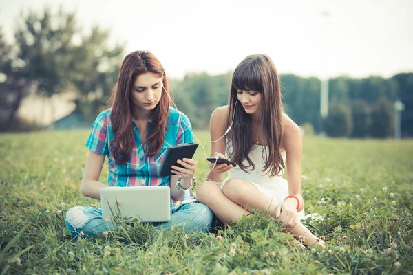 Irmãs usando tablet e smartphone no parque — Fotografia de Stock