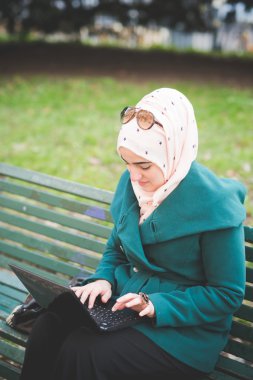 muslim woman at  park with laptop clipart