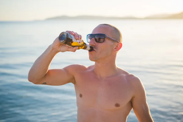 Человек пьет пиво на пляже — стоковое фото