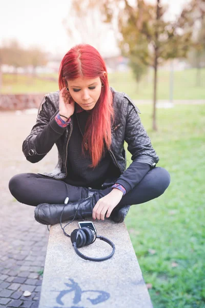 Jeune femme assise dans le parc avec écouteurs — Photo