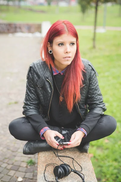 Jovem sentada no parque com fones de ouvido — Fotografia de Stock