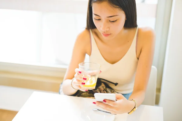 Woman drinking a juice and using a smartphone — Stockfoto