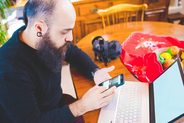 Uomo barbuto sul tavolo utilizzando smartphone — Foto Stock