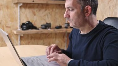 Yetişkin Adam Freelancer bilgisayarını kullanarak evden internete bağlanıyor, bilgisayarda daktilo yazıyor, internetten ekrana bakıyor ve uzak işlerden keyif alıyor.