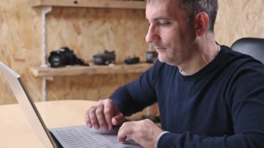 Yetişkin Adam Freelancer bilgisayarını kullanarak evden internete bağlanıyor, bilgisayarda daktilo yazıyor, internetten ekrana bakıyor ve uzak işlerden keyif alıyor.