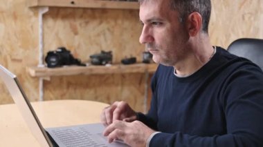 Yetişkin Adam Freelancer bilgisayarını kullanarak evden internete bağlanıyor, bilgisayarda daktilo yazıyor, internetten ekrana bakıyor ve uzak işlerden keyif alıyor.