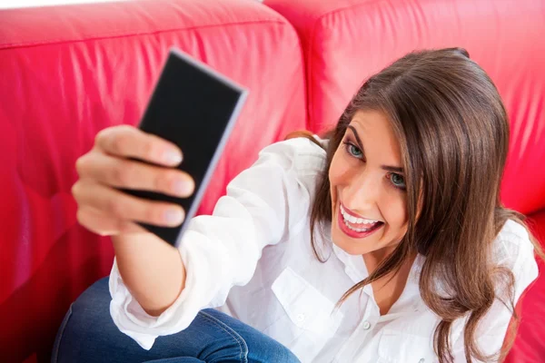 Young woman making face while taking selfie on sofa — Stock fotografie