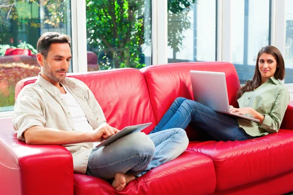 Young couple using digital tablet and laptop on sofa — Stok fotoğraf