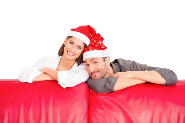 Felice coppia indossa cappelli di Babbo Natale dietro il divano rosso Fotografia Stock