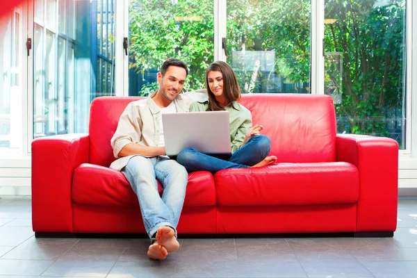 Счастливая молодая пара с ноутбуком на красном диване Стоковое Фото