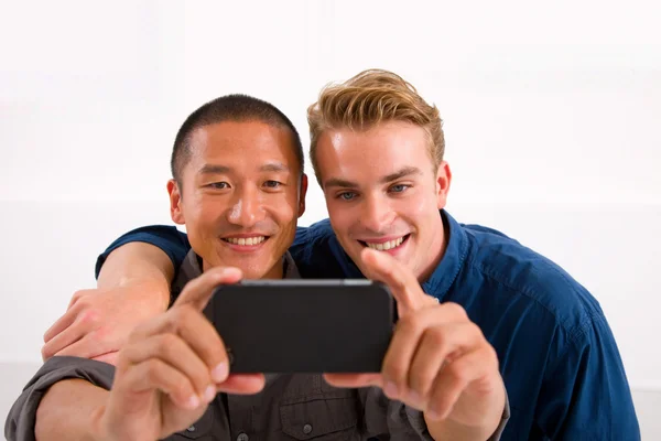 Deux jeunes hommes souriants prenant autoportrait avec téléphone cellulaire — Photo