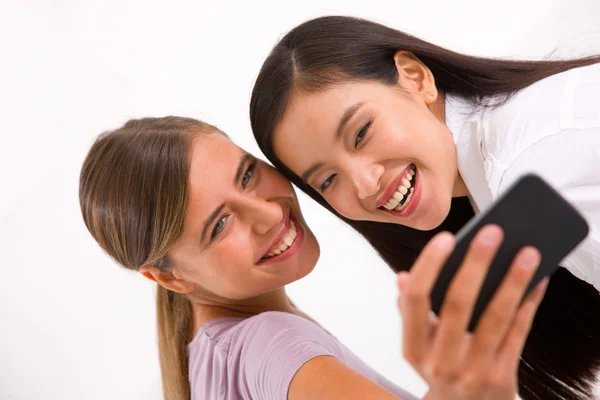 Two smiling young women taking self portrait with cell phone — Stock Photo, Image