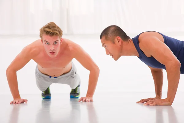 Two young male doing push-ups in gym — Stock Photo, Image