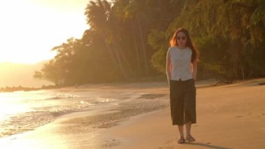 Gün batımında tropik sahilde yürüyen Asyalı kadın..