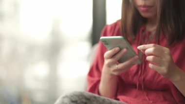 Genç Asyalı kadın kafeteryada sosyal medya için akıllı telefon kullanıyor..